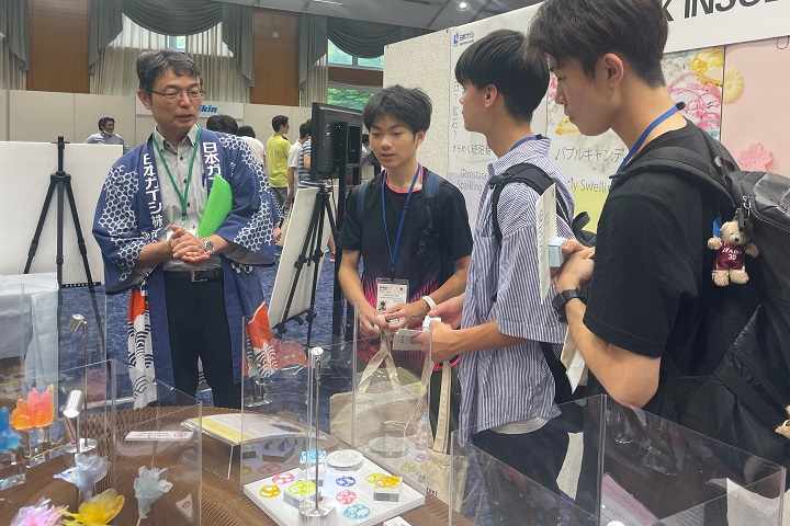 日本ガイシブースを訪れた日本代表選手団に、製品やNGKサイエンスサイトの展示品を紹介する社員